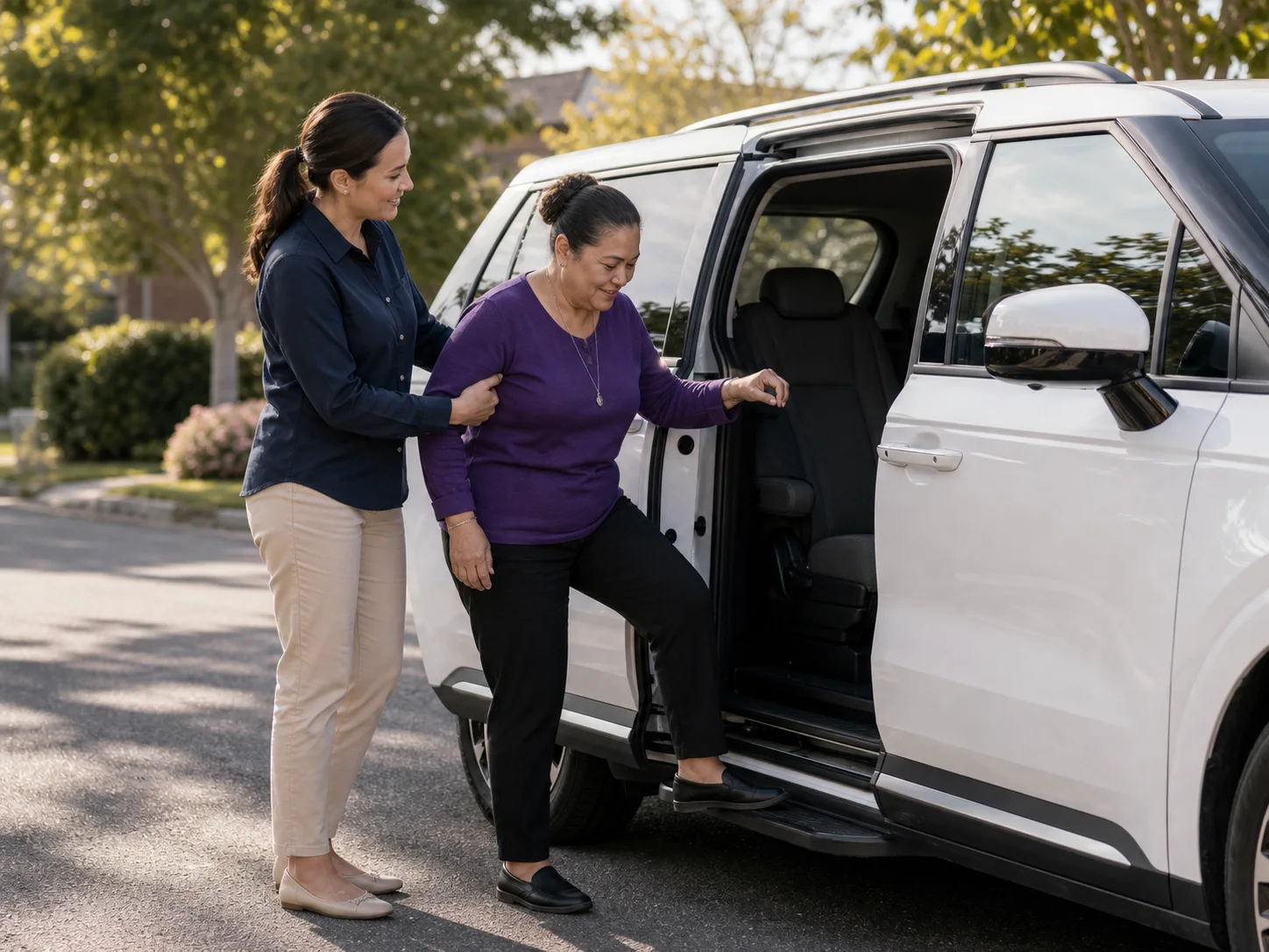 An adult passenger receiving respectful assistance beside a white Kia Carnival